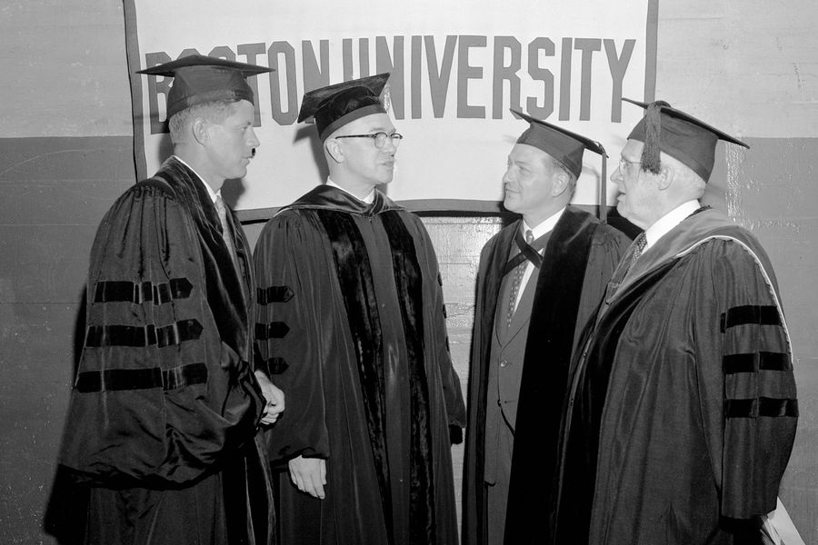 Photo: A black and white photo of United States Senator John F. Kennedy (D-Mass) (left) and Harvard President Nathan M. Pusey, shown flanking BU President Harold Case, received honorary degrees at BU Commencement. They are in ceremonial garb, talking amongst themselves.