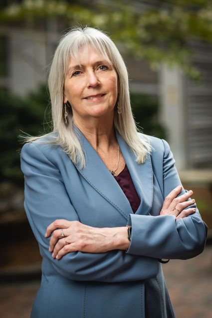 Photo: A portrait of Patricia (Trysha) Ahern, a white woman with longer, lighter gray hair and bangs. She wears a pale blue blazer and a purple blouse.