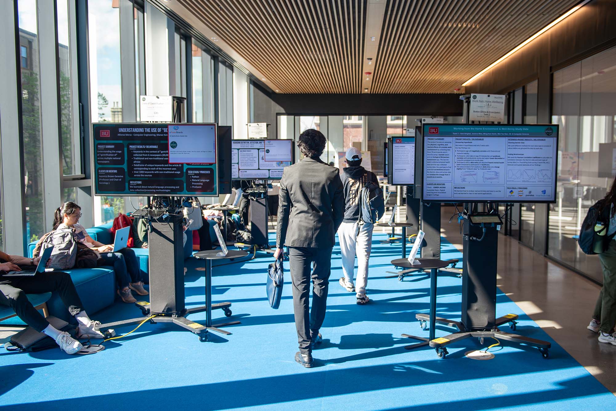 Photo: A person in a suit holding a briefcase walks in between two large monitor screens at what appears to be a tech conference or corporate gathering