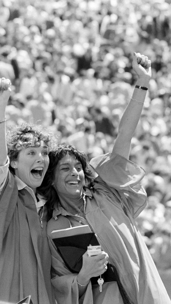 Photo: Two women wearing red robes raise their fists in excitement for a posed photograph in front of a large crowd at Boston University's commencement on Nickerson Field on May 17, 1981