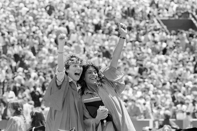 Photo: Two women wearing red robes raise their fists in excitement for a posed photograph in front of a large crowd at Boston University's commencement on Nickerson Field on May 17, 1981