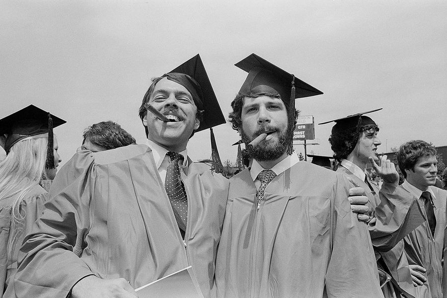 Photo: Two male graduates wearing ties, red robes, and black caps, celebrate with cigars at the Boston University Commencement on Nickerson Field on May 16, 1982.