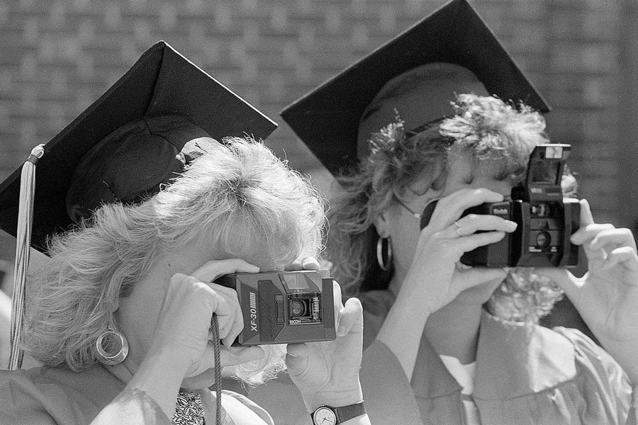 Photo: Two female graduates with big hair take photos on large film cameras after the Boston University Commencement on Nickerson Field on May 15, 1988.