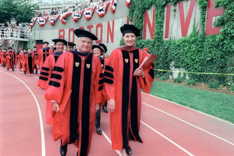 Photo: Geena Davis, a white woman wearing red regalia leads a procession of others in similar red robes, walking out of Commencement Ceremonies after receiving an honorary degree on May 23, 1999
