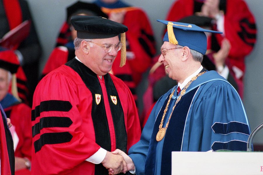 Photo: Thomas Menino, a white man wearing wireframe glasses, a red and black ceremonial graduation gown and black beret, shakes hands with Boston University President Jon Westling, a white man with greying black hair wearing glasses, a blue ceremonial gown, and large gold medallion.