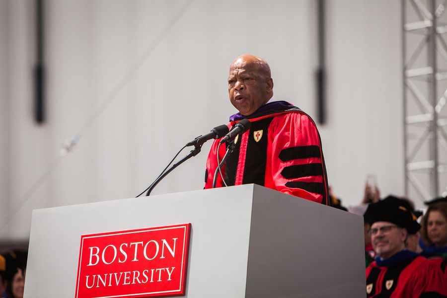 Photo: John Lewis, an older bald Black man wearing a red and black ceremonial graduation gown, delivers the commencement address during the 2018 Boston University Commencement on Nickerson Field on May 20, 2018.