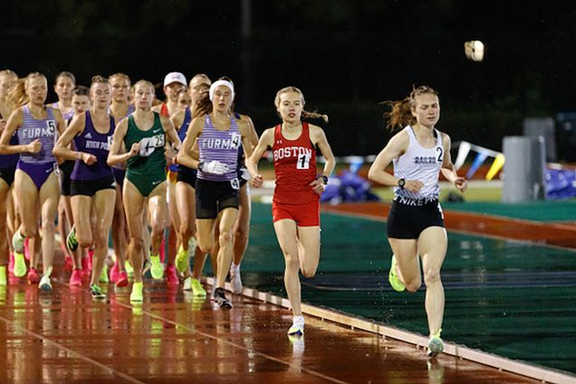 Photo: A group of runners at the Patriot League move forward on an outdoor track. They are all wearing a typical track uniform which is a tank and shorts. Coming up behind the lead is Daisy Liljegren (CAS’24, Sargent’24).