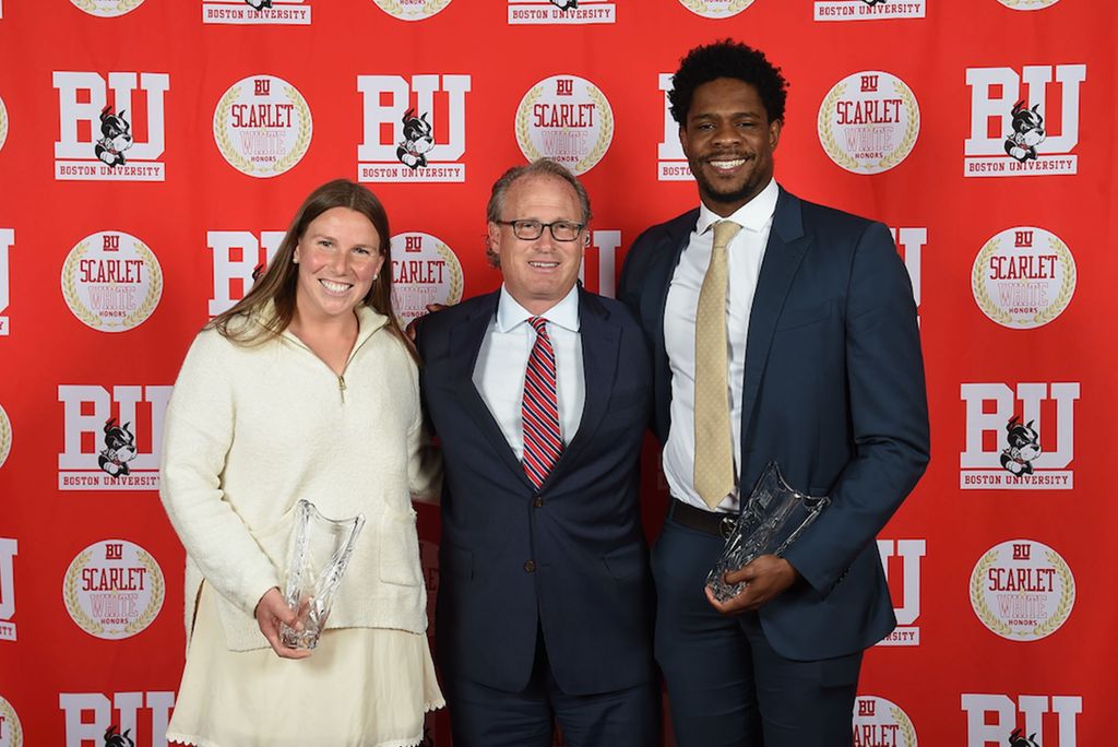 Photo: Three young people wearing formal clothing smile for a photo at an athletic banquet at Boston University. They are standing in front of a red BU background.