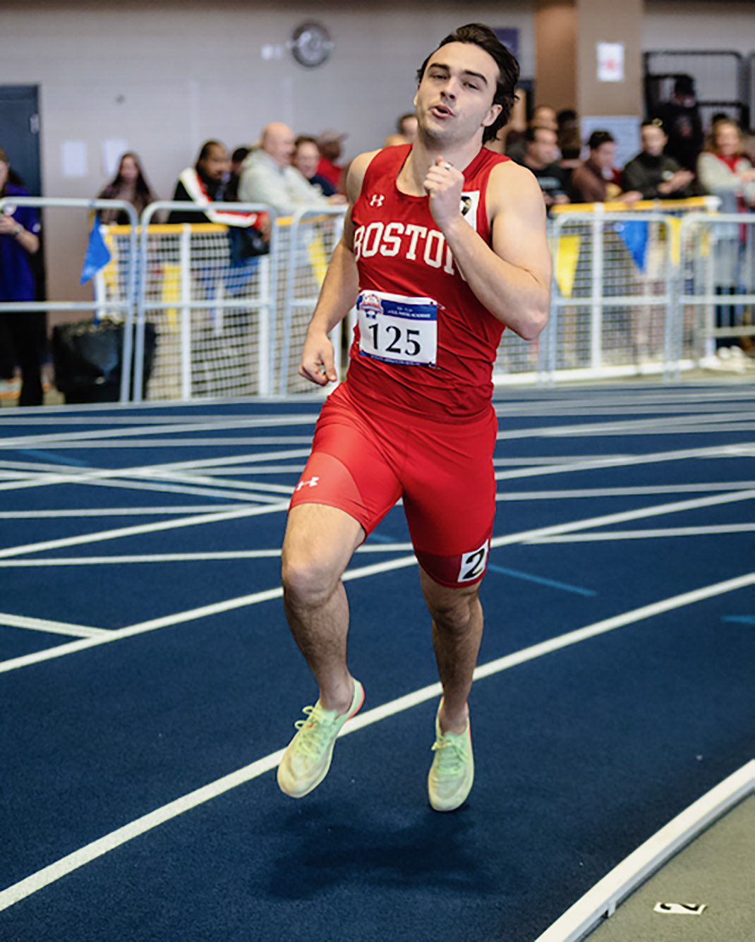 Photo: A male runner in an all red uniform runs on an indoor track.