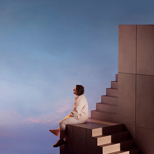 Image: Album cover for Lewis Capaldi's "Broken by Desire to Be Heavenly Sent". A person is seen sitting on the edge of a set of precarious stairs as they make a sharp turn to the right. The sky during sunset can be seen around the stairs.