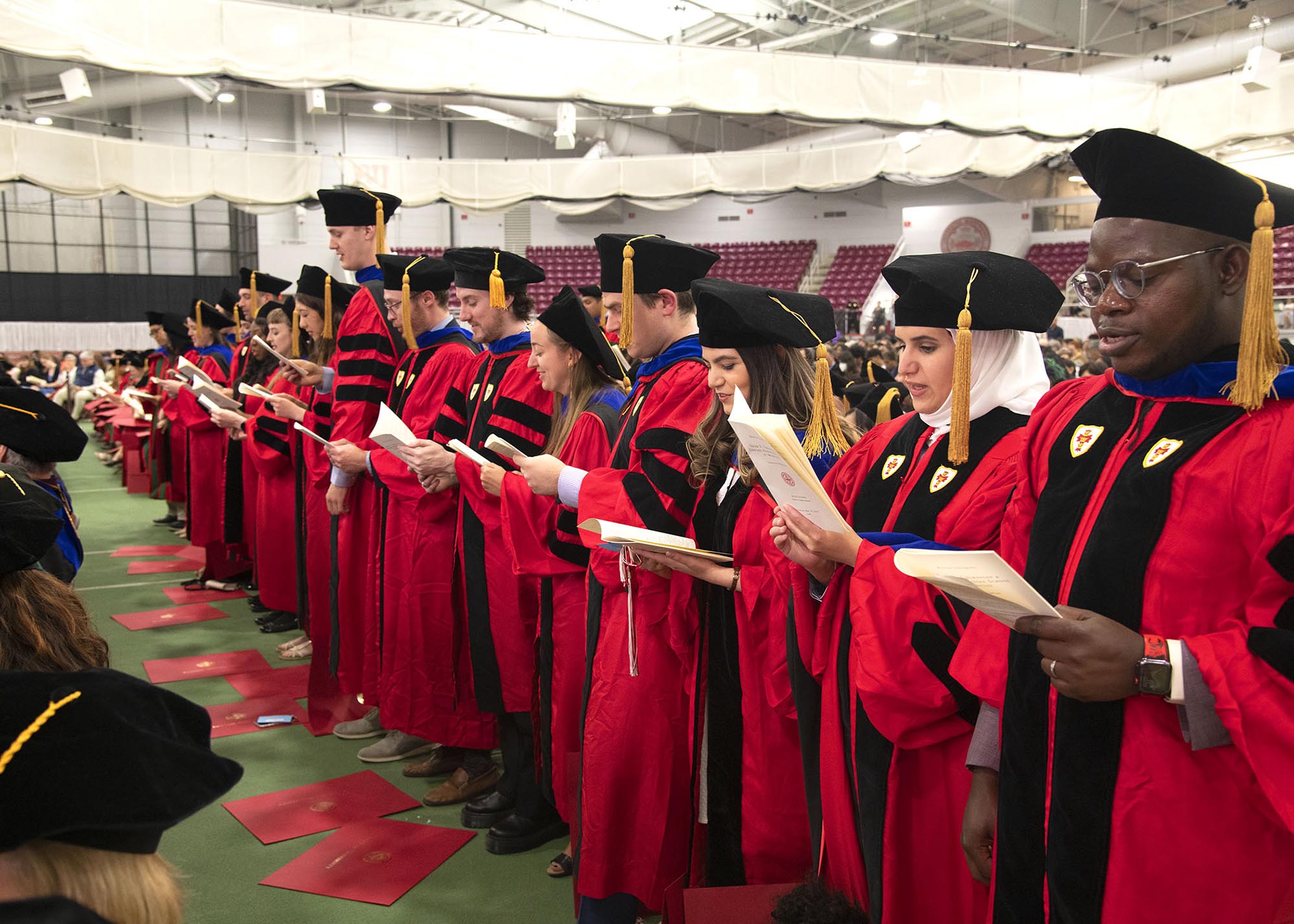 Photo: Students wearing red graduation gowns, black and blue stoles, and black graduation caps stand and read the hippocratic oath.