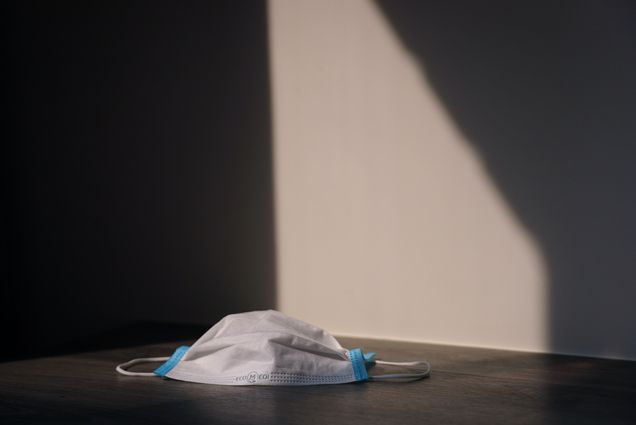 Photo: A long medical-grade face mask is shown illuminated in a dark room. Scene has a somber mood.