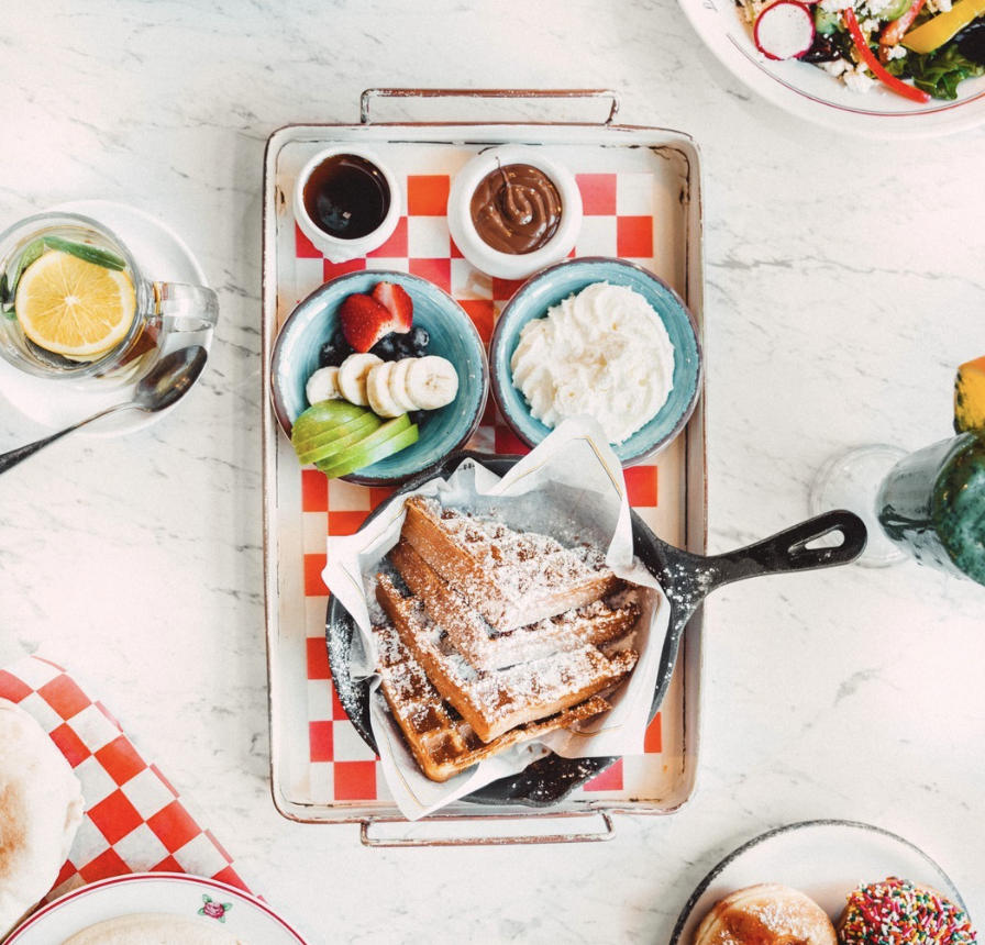 This is a photo of food served at Cafe Landwer in Boston. It is a breakfast dish with waffles, fruit, whipped cream, and other breakfast pickings.