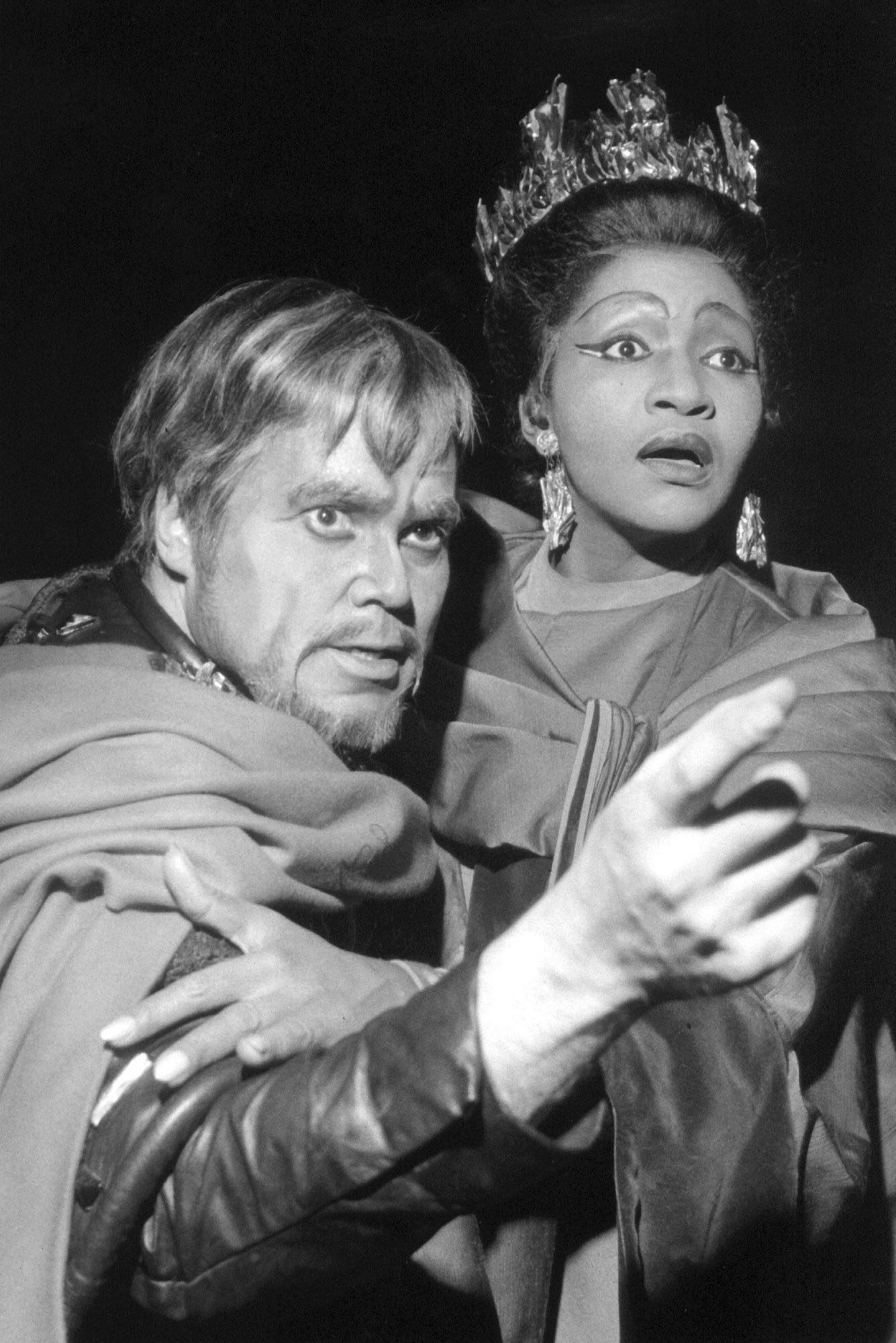 Photo: Grace Bumbry performing at the Verdi opera house in Germany. To her left is baritone Dietrich Fischer-Dieskau. They have on dramatic stage makeup and look to the right of the photo, in shock. The photo is in black and white.