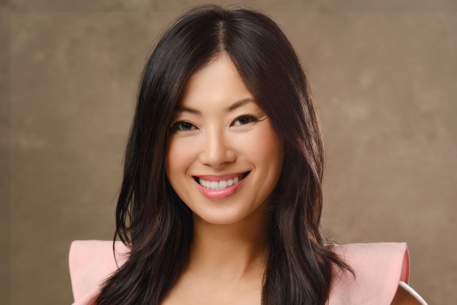 Photo: Jennifer Yen, an Asian woman with long black hair wearing a pink top, stands in front of a generic photo drop and smiles for the camera.