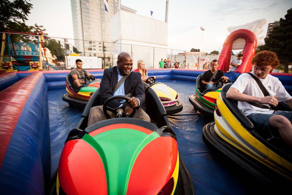 Ken Elmore driving a colorful bumper car. He smiles, and wears a suit, as he and BU students drive around.