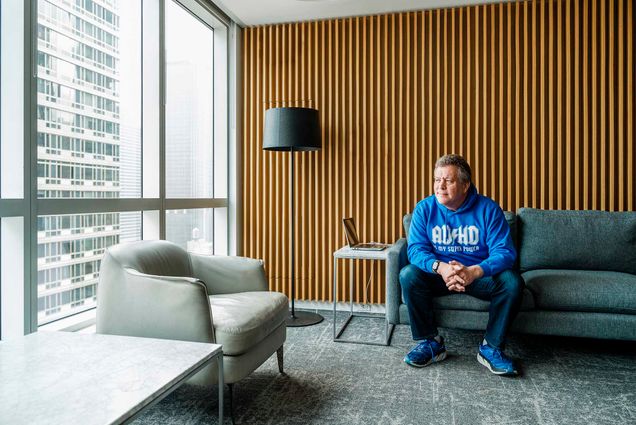 Photo: A man in a blue sweater sits on a modern leather couch staring out the window in NYC. Peter Shankman (CGS’92, COM’94), author of a new children's book on neurodiversity. Photo by Chris Sorensen for Boston University Photography.