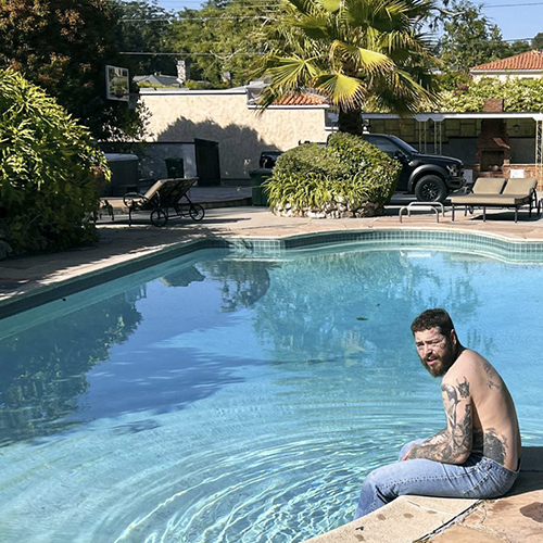 Image: Album cover for Post Malone's "Austin". Post Malone, a white man wearing light blue swim trunks, sits at the edge of a pool and looks to the camera. A house can be seen behind the pool.