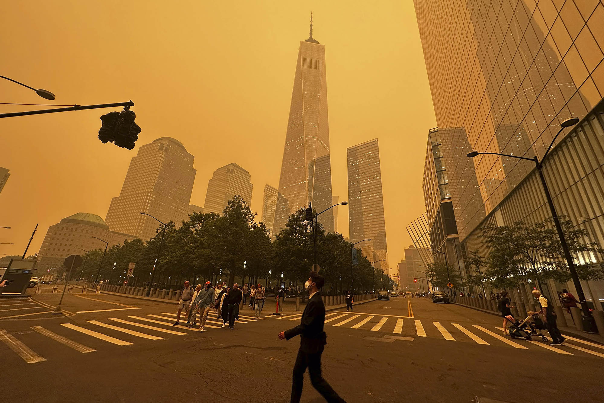Photo: Pedestrians pass the One World Trade Center, center, amidst a smokey haze from wildfires in Canada. Scene is tinted a sepia-orange as masked pedestrians walk in and around the city.