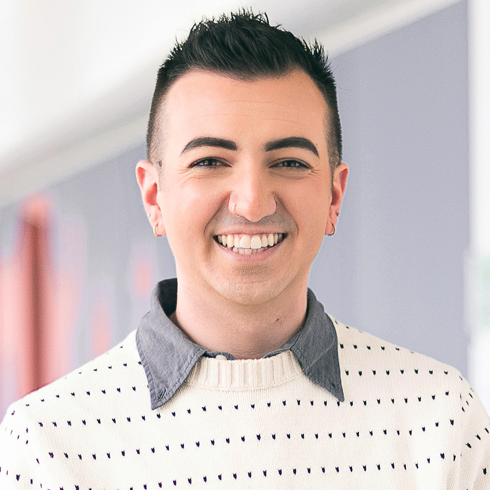 Photo: Jesse Moreira, a person with dark spiky hair and a nice smile wearing a white dotted sweater and gray collared shirt