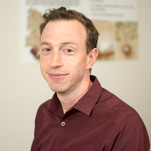 Photo: Headshot of Jesse Mez, a white man with short, curly brown hair wearing a burgundy collared shirt.