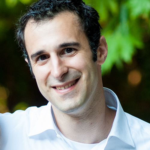 Photo: Michael Economo, a white man with short black hair and wearing a white collared shirt, smiles and poses in front of greenery.