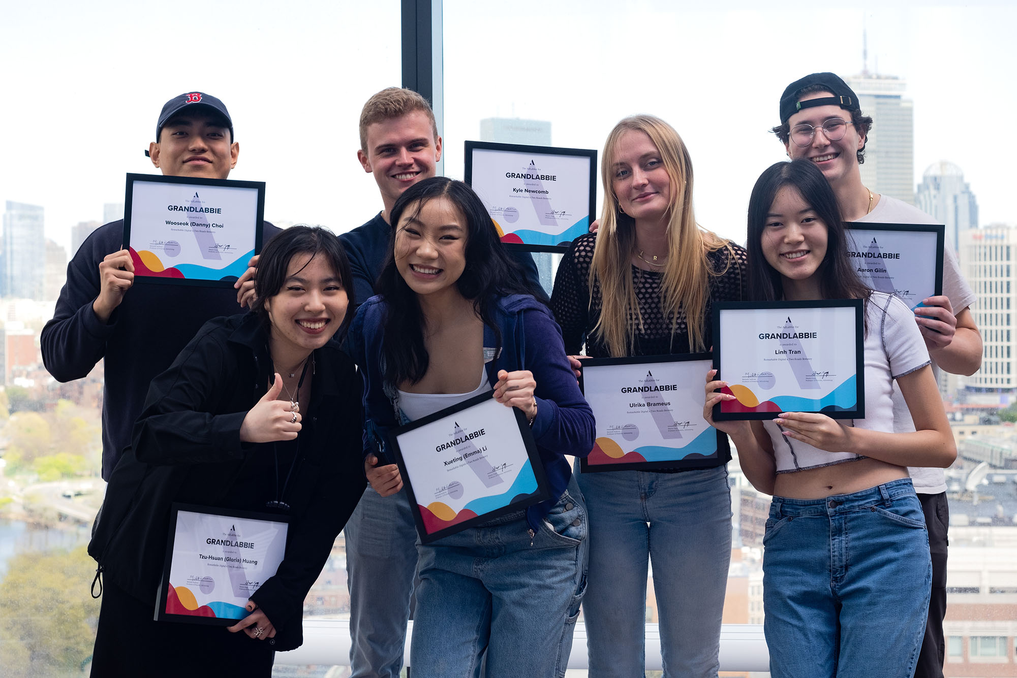 Photo: Group photo of various students standing in front of a large window and smiling and holding up certificates that read "Grandlabbies".