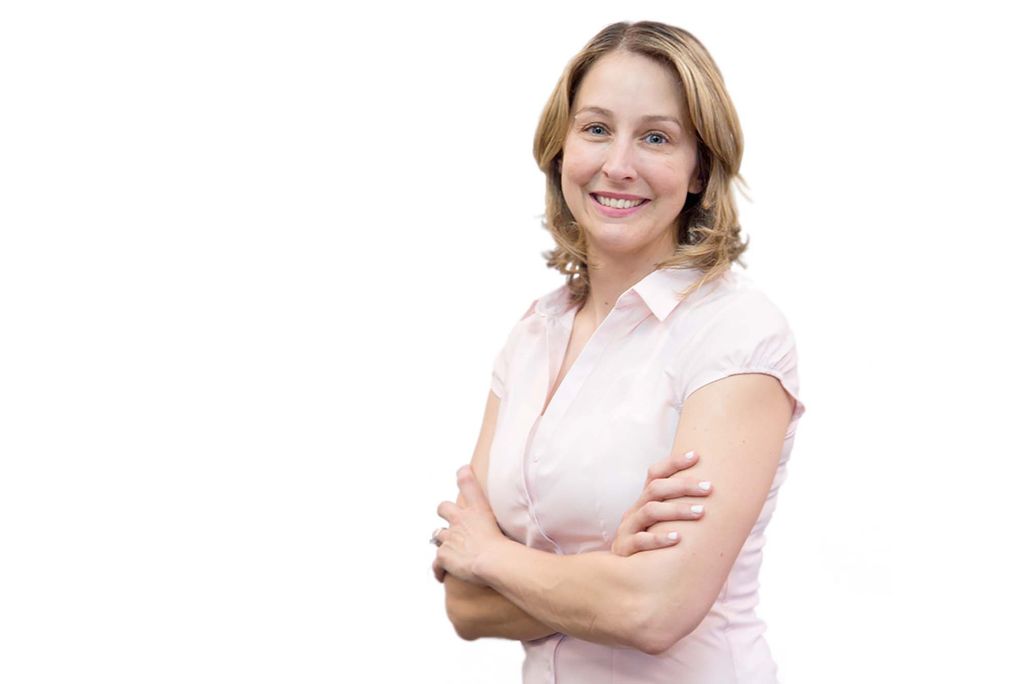 Photo of Naomi Mann, a white woman with short blonde hair posing with her arms crossed on a white background. She smiles and wears a light pink short-sleeve blouse.