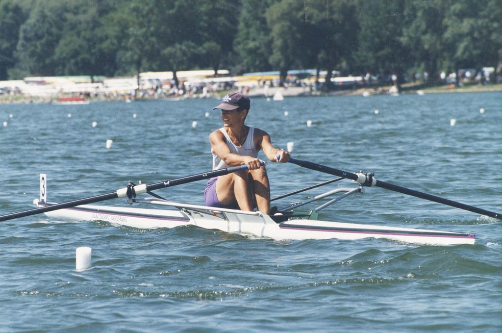 Film photo of Jeanne Friedman (Sargent’75), a member of the BU women’s rowing team in its last year as a club sport before it became a varsity team. She is picture in a blueish hat and white tank top rowing in a single boat on a river with small white caps.