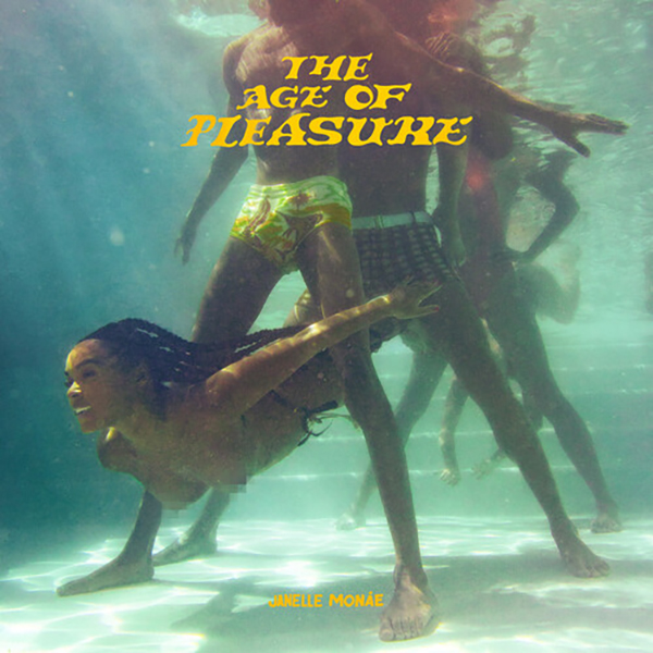 Photo: Black woman swimming through legs underwater in a pool. She is topless with long braids and swims to the left of the shot. There are two men and one woman, the men are wearing swim trunks and the woman is wearing a full-suit.