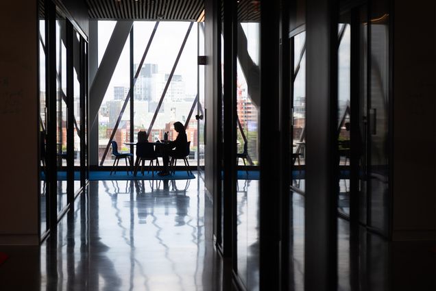 A person sits in a chair with a large array of windows with cityscape behind them.Johana Chaparro (Wheelock’25) enjoys the view from one of the upper floor study areas in CDS on June 29, 2023. Photo by Cydney Scott