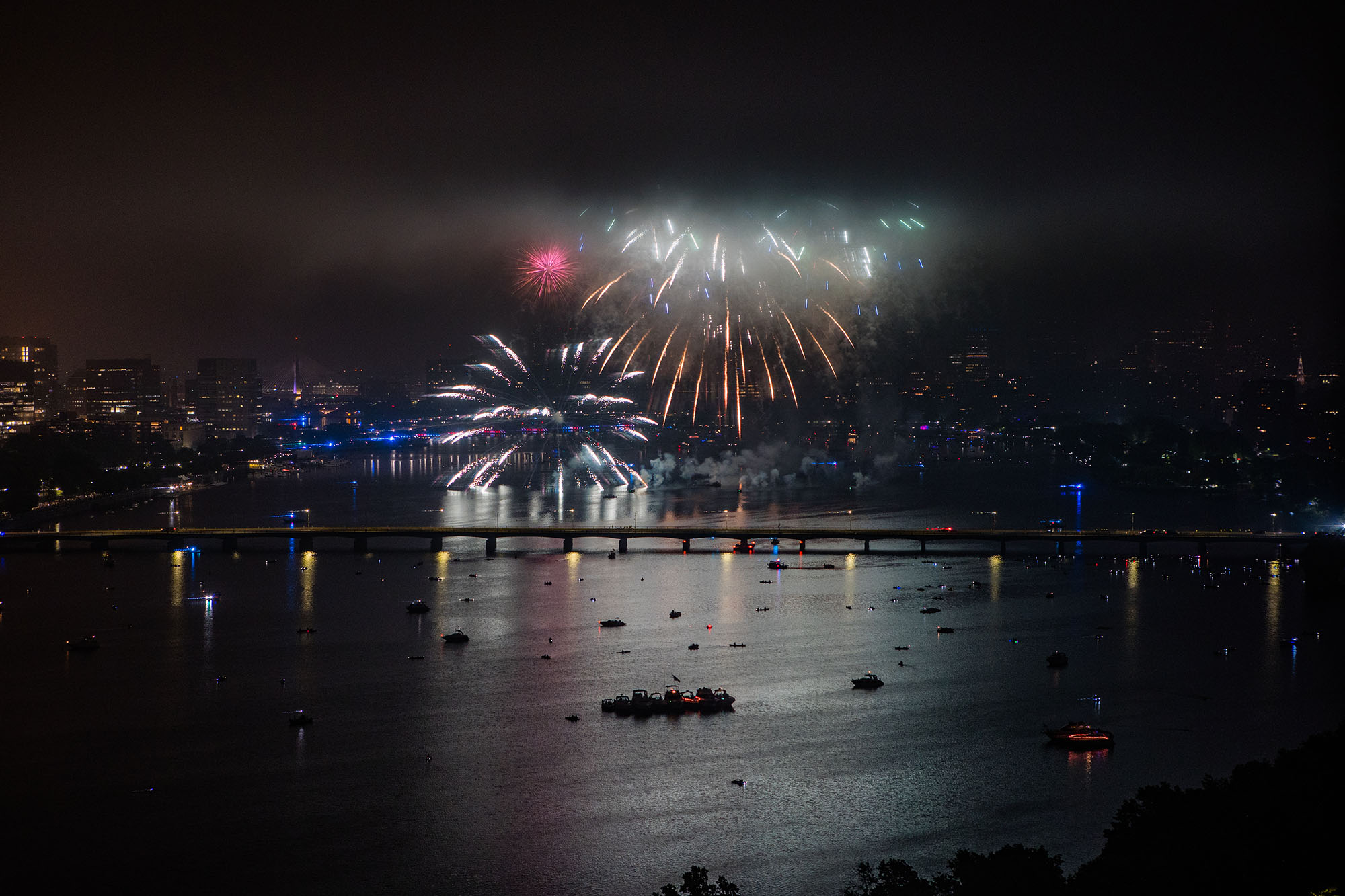 Photo: 4th of July fireworks are shown going off on a dark night above the Charles river. White and yellow fireworks light up the night sky and show the Boston skyline.