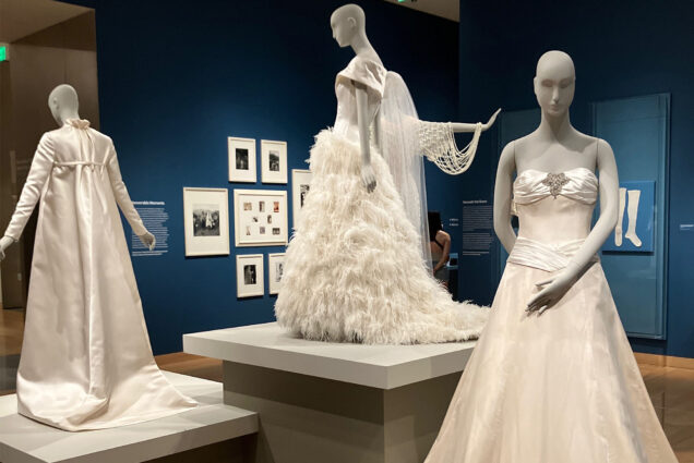 Photo: Three mannequins wearing wedding dresses with small plaques on the wall behind them