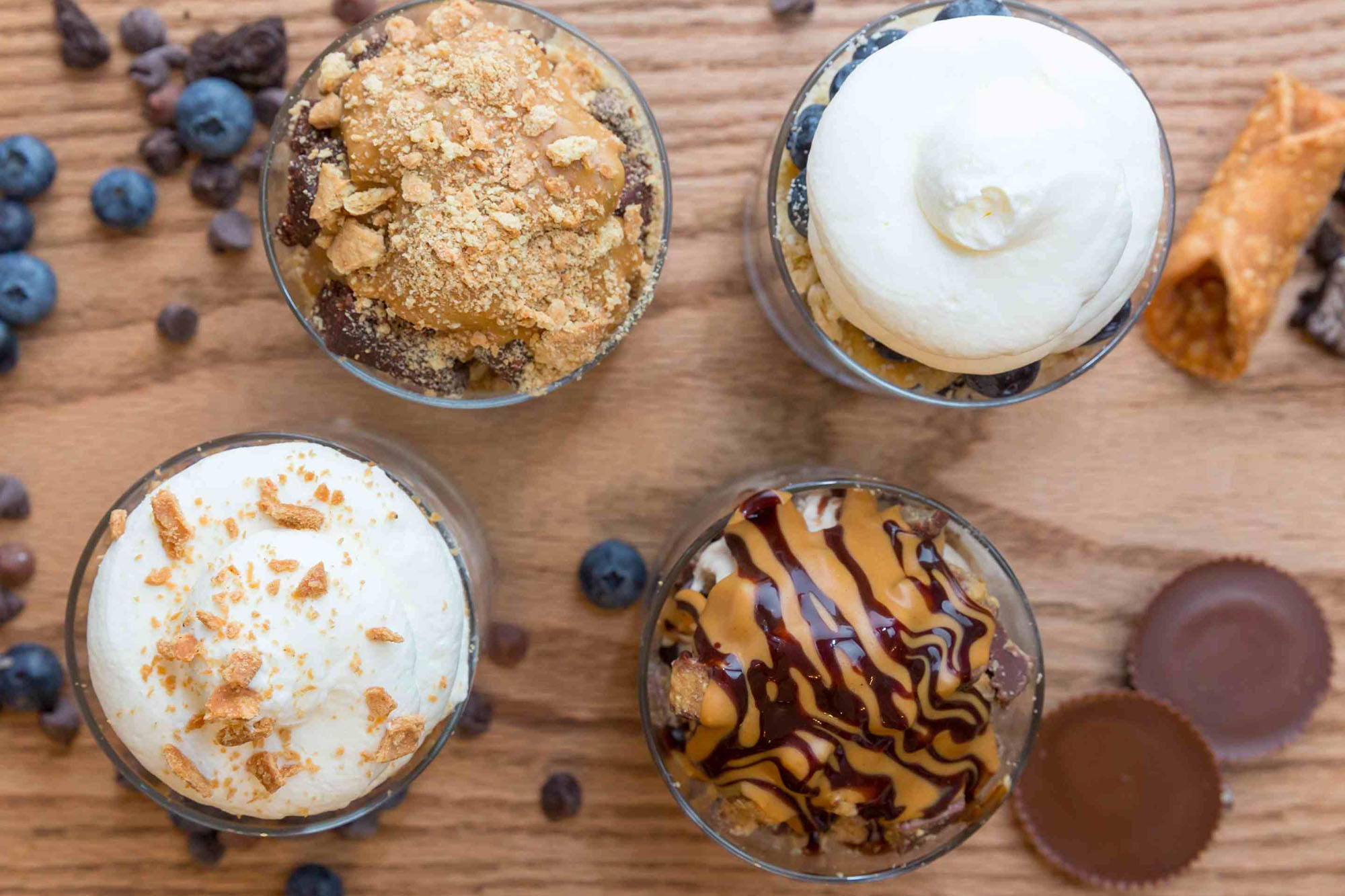 Photo: Four different containers hold ice cream flavors with different toppings in a flat lay ontop of a wooden table.