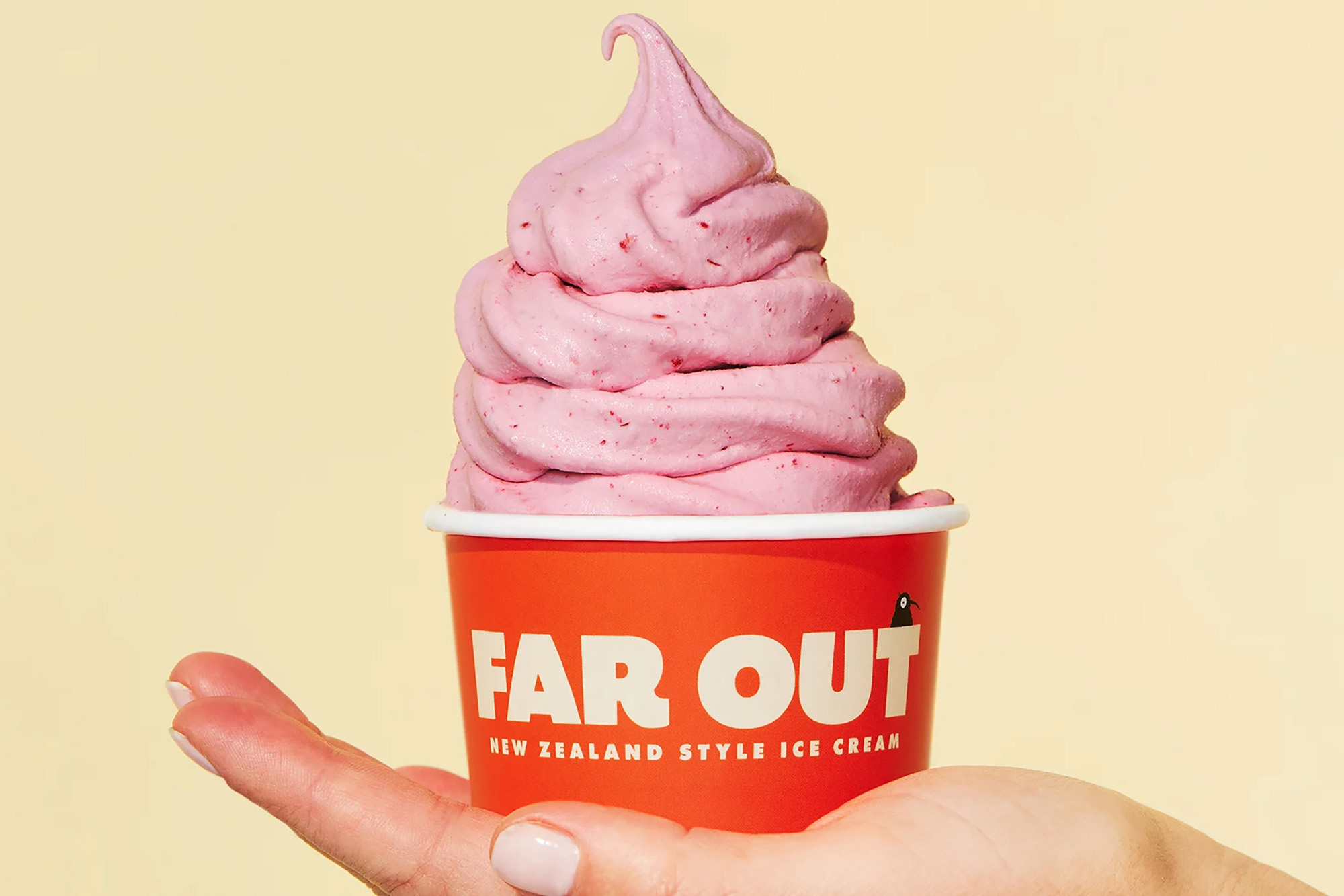 Photo: A white hand holds a red cup with pink swirled ice cream in front of a pale yellow background.