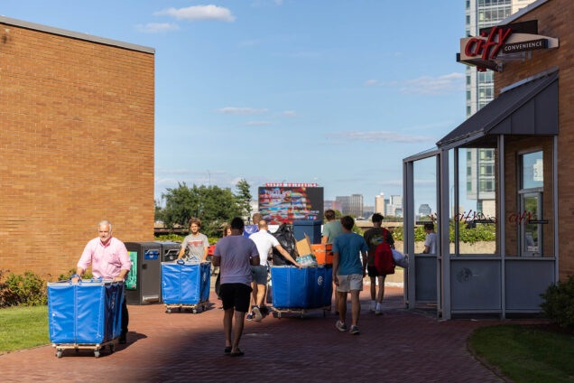 Photos: Students are shown moving in to West Campus dorms dorms on Boston University's Campus. Various students and people push large blue carts filled with various items and suitcases.