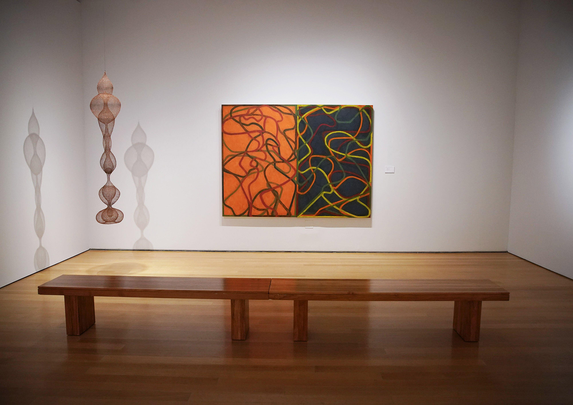 Photo: A white gallery wall shows a large canvas half the canvas and the other half is dark blue. Yellow and red squiggles fill the canvas as well. an abstract hanging is also shown to the left of the canvas.