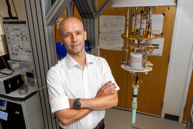 Photo: A bald man in a white collared short sleeve shirt stands with arms crossed