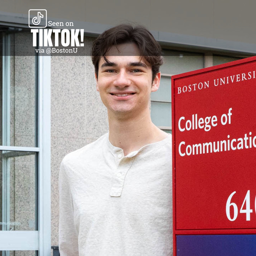 Photo: A white man stands outside in a white mock button up. He stands next to a BU sign that reads COLLEGE OF COMMUNICATION 640.