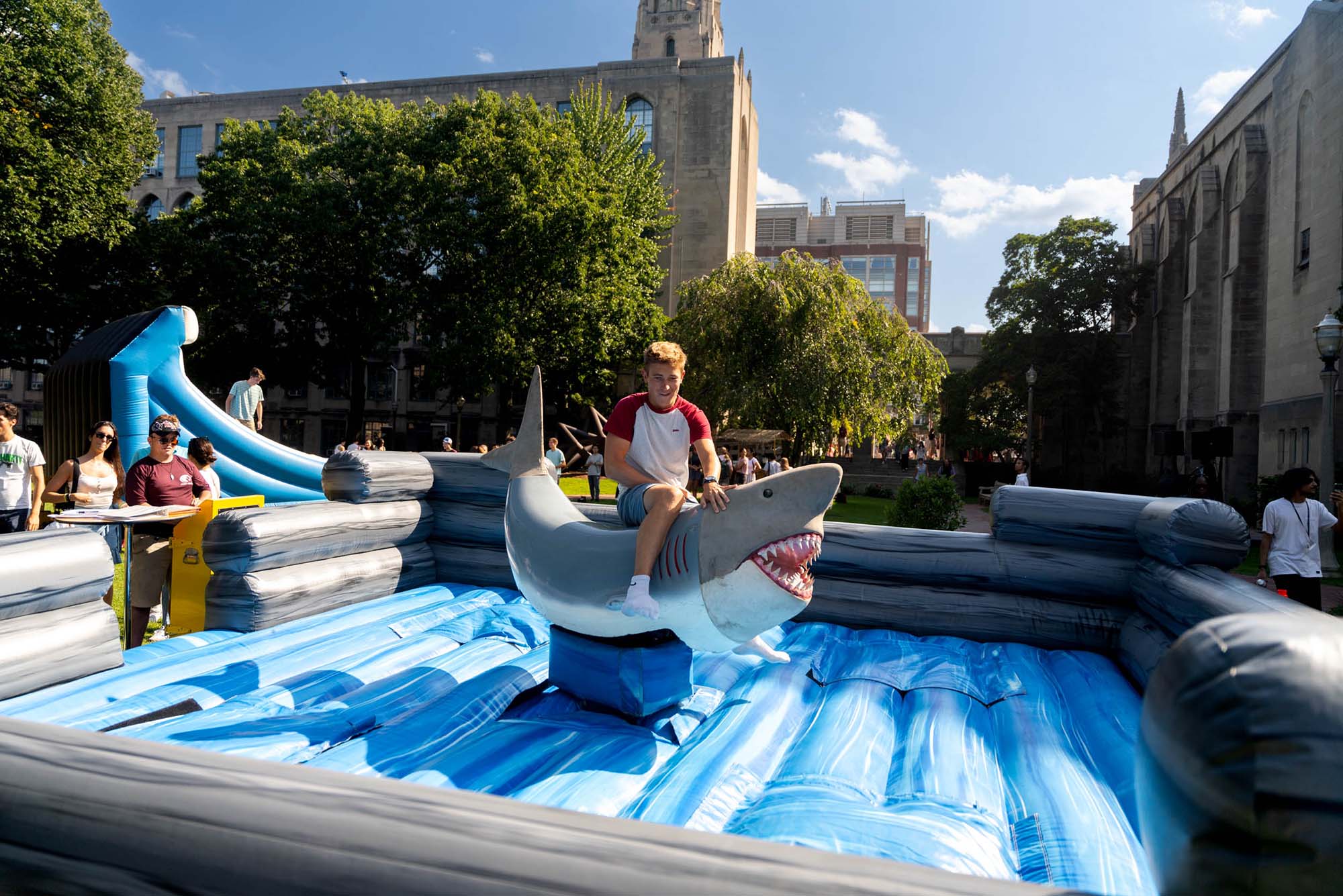Photo: A young man wearing a white and red shirt and jeans shorts rides an inflatable shark in a large inflatable structure.