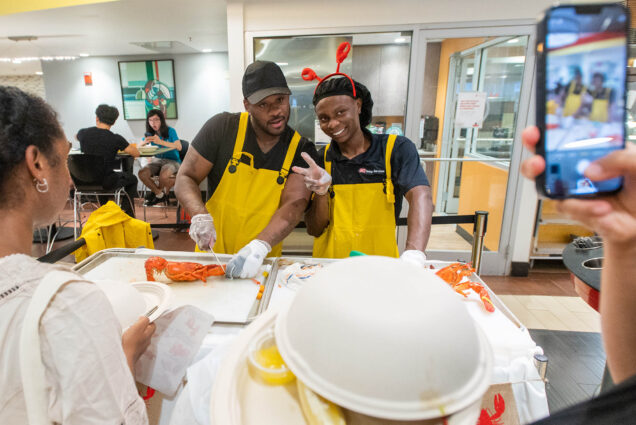 Photo: Two dining hall works poses together as they work on preparing red lobsters for students in the dining hall.