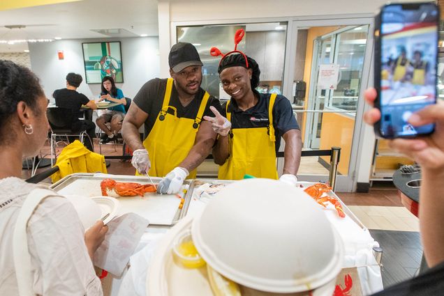 Photo: Two dining hall works poses together as they work on preparing red lobsters for students in the dining hall.