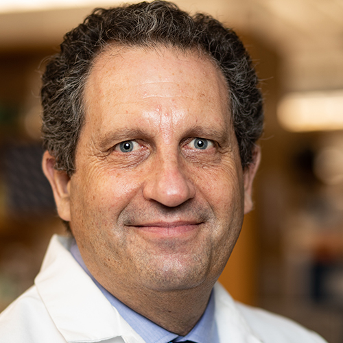 Photo: Headshot of Darrell Kotton. A white man with dark brown hair and wearing a light blue collared shirt and white lab coat smiles and poses for the camera.