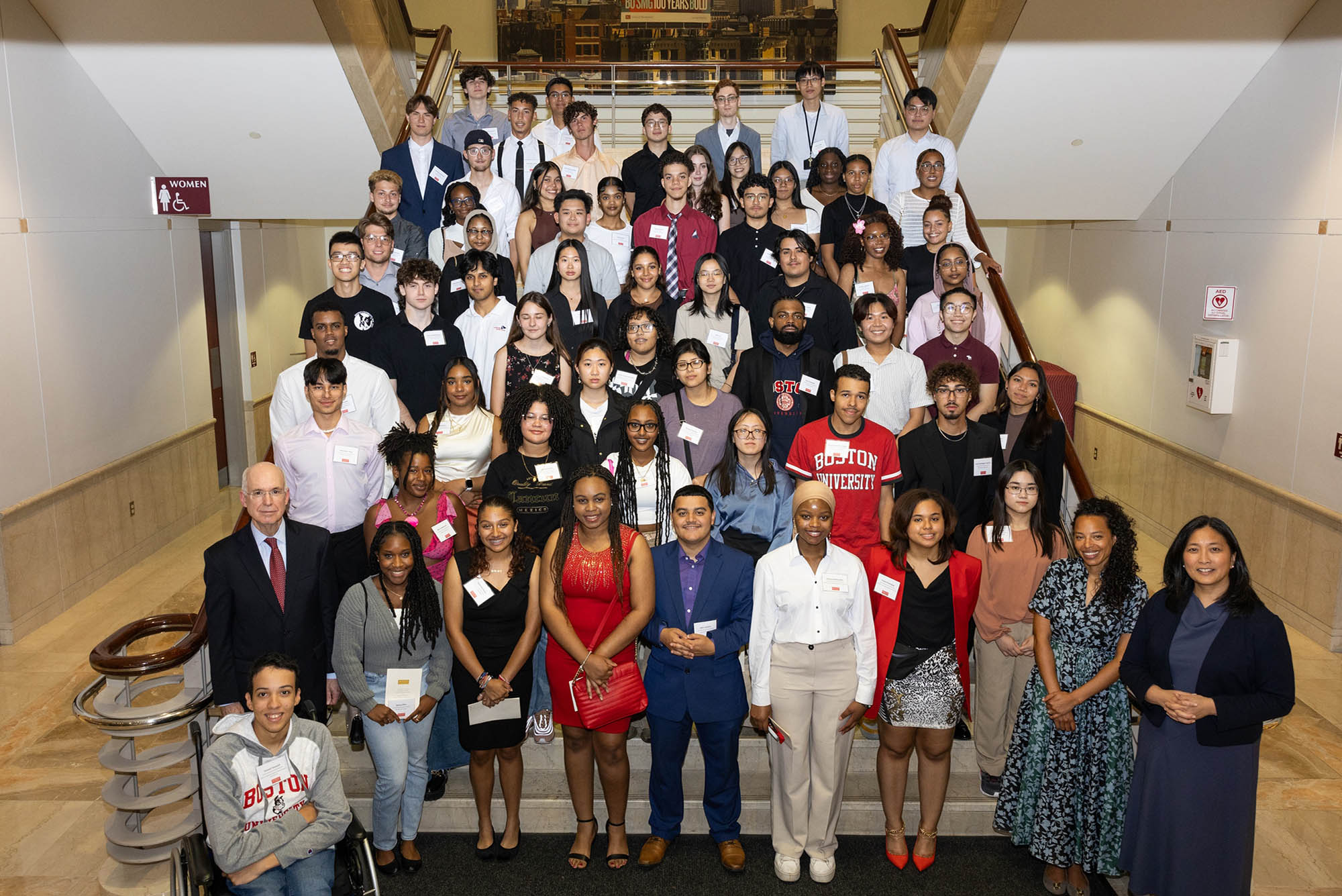 Photo: Large overhead shot of 2023's Menino Scholarship and ComCommunity Service Award recipients. Students in business casual attire pose on a large set of stairs together. Also pictured are interim President Ken Freeman.