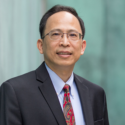 Photo: Weining Lu, am older Asian man wearing glasses, a light blue collared shirt, red tie, and black blazer, smiles and poses in front of a blurred, green background.
