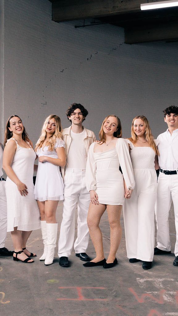 Photo: Members of BU's acapella group, Trebelmakers, stand in a land for a group shot. They are in a warehouse and all members are wearing personal variations of a white outfit. They are stand, candidly.