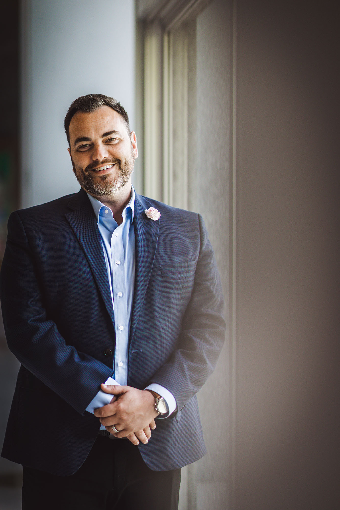 Photo: A portrait of Jason Campbell-Foster, a white man with graying hair and beard, stands with his hands clasped and smiling at the camera. He wears a blue suit and a blue button up.