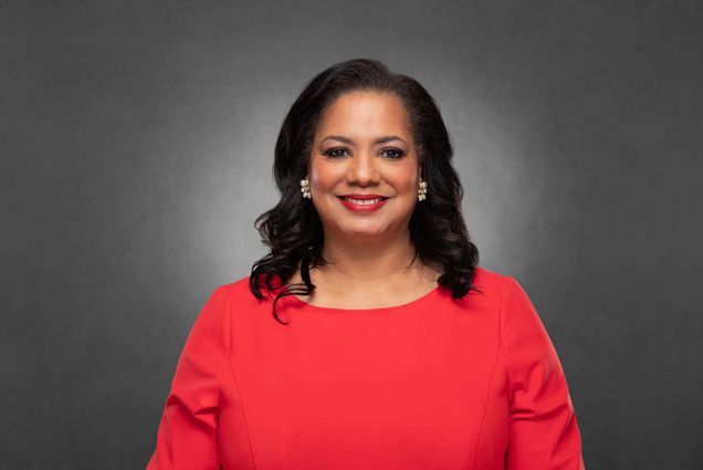 Photo of Antoinette “Tonie” Leatherberry (ENG’85), a middle-aged Black woman with shoulder length, slightly curled dark hair. She smiles, wears read lipstick, and earrings in the shape of a flower. She wears a pinkish-orange dress and stands in front of a dark gray background.