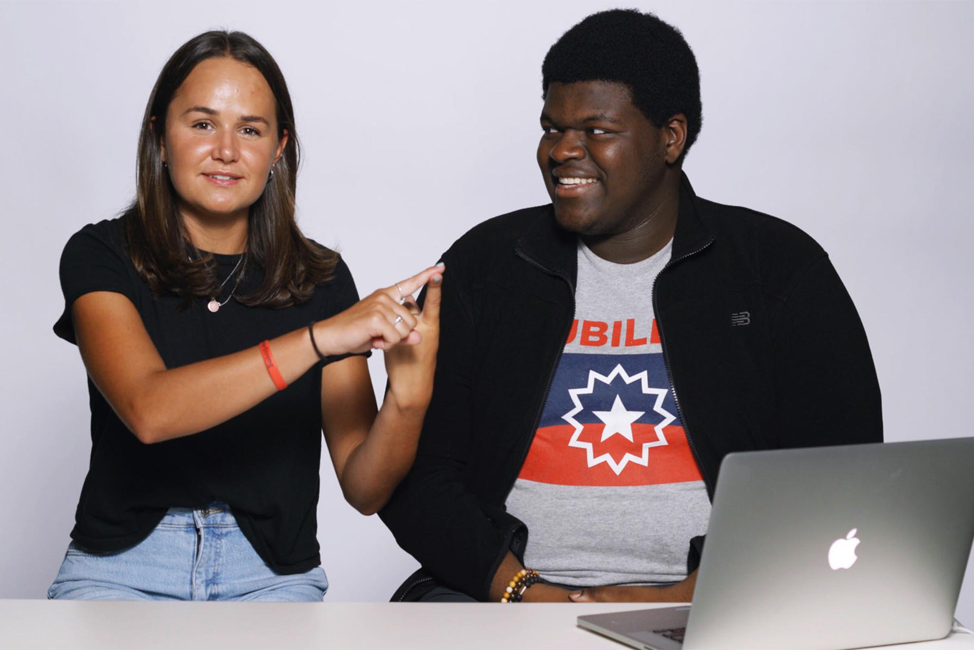 Photo: Two students in casual clothing sit next to each other while having a discussion. One student has a laptop open in front of them.
