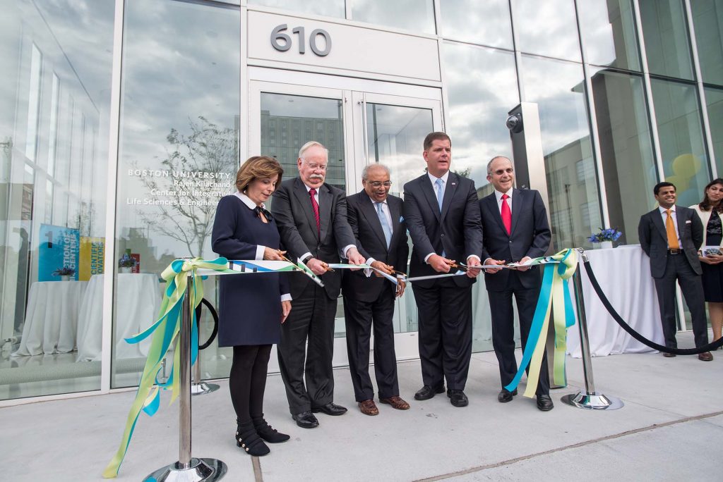 Ribbon cutting of CILSE by Gloria Waters, BU VP (from left), Robert A. Brown, BU president, trustee and benefactor Rajen Kilachand (Questrom’74, Hon.’14), Martin J. Walsh, Boston mayor, and Kenneth J. Feld (Questrom’70), Board of Trustees chair. They each hold large scissors and cut a blue and green ribbon. The silver entrance to the windowed building is seen behind them, it bears the number 610.